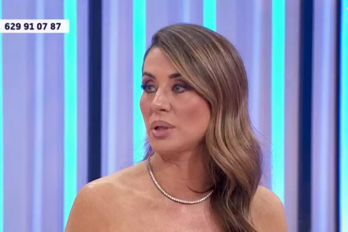 Elena Tablada con cabello largo y ondulado mira hacia un lado en un entorno con luces verticales azules y moradas. Elena Tablada con cabello largo y ondulado mira hacia un lado en un entorno con luces verticales azules y moradas.
