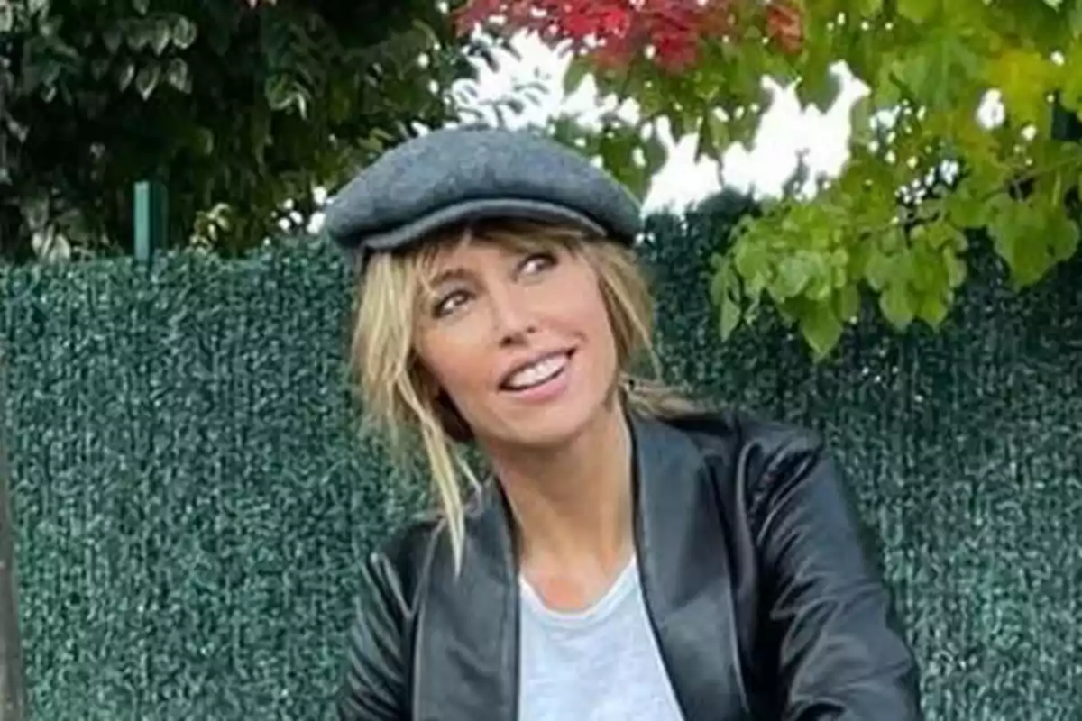 Emma García con boina gris y chaqueta de cuero negro sonríe mientras está sentada al aire libre con un fondo de vegetación. Emma García con boina gris y chaqueta de cuero negro sonríe mientras está sentada al aire libre con un fondo de vegetación.