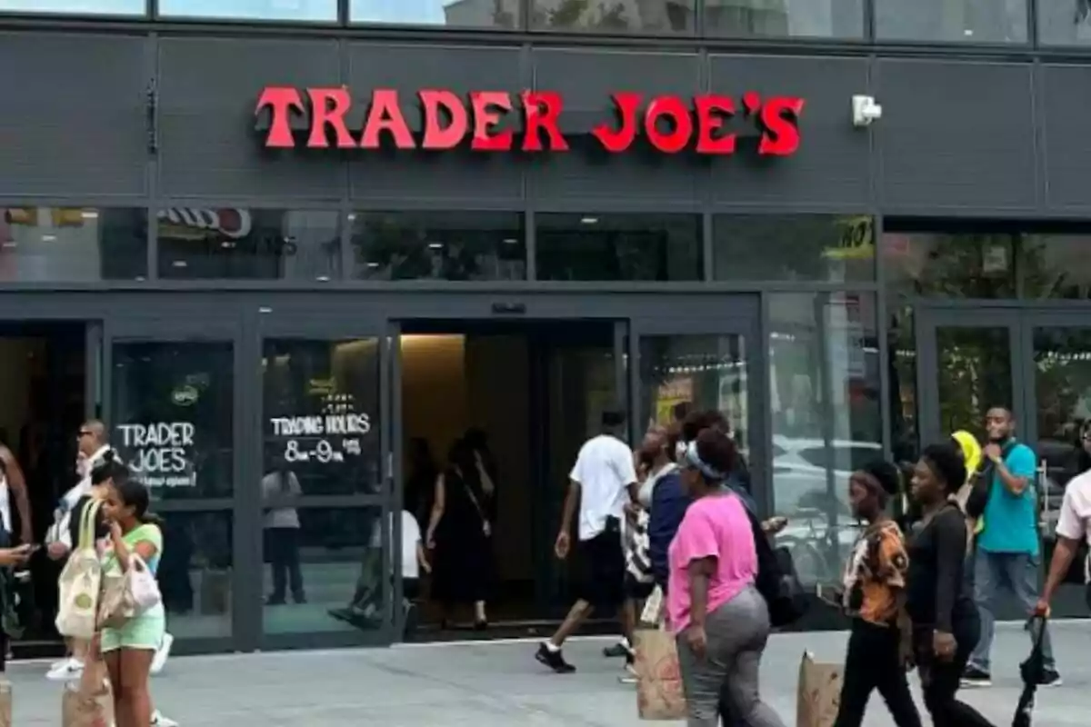 Fachada de una tienda Trader Joe's con varias personas entrando y saliendo mientras llevan bolsas de compras. Fachada de una tienda Trader Joe's con varias personas entrando y saliendo mientras llevan bolsas de compras.