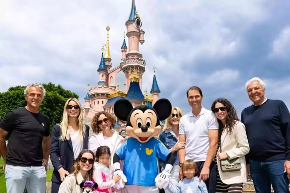 A group of people smiles next to a person dressed as Mickey Mouse in front of a castle at a Disney theme park under a cloudy sky. A group of people smiles next to a person dressed as Mickey Mouse in front of a castle at a Disney theme park under a cloudy sky.