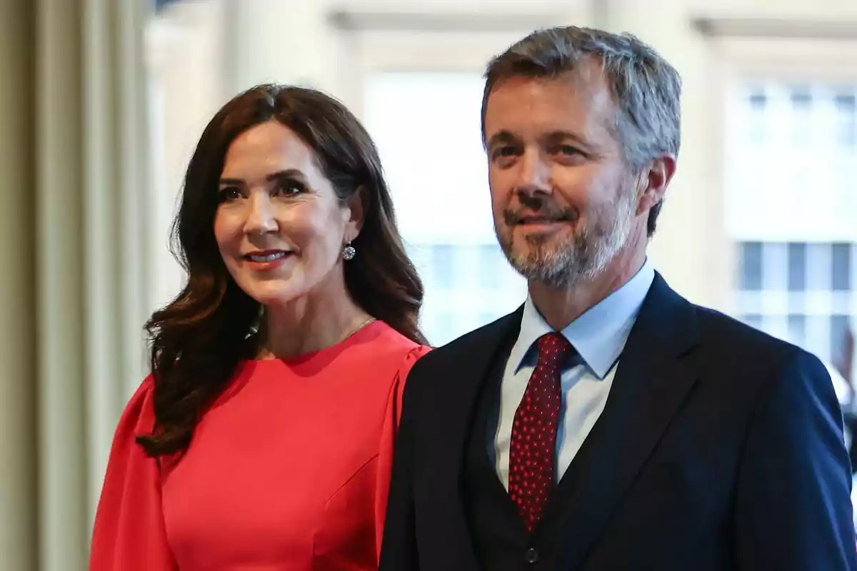 Una mujer con vestido rojo y un hombre con traje oscuro y corbata roja posan juntos sonriendo en un entorno interior iluminado. Una mujer con vestido rojo y un hombre con traje oscuro y corbata roja posan juntos sonriendo en un entorno interior iluminado.
