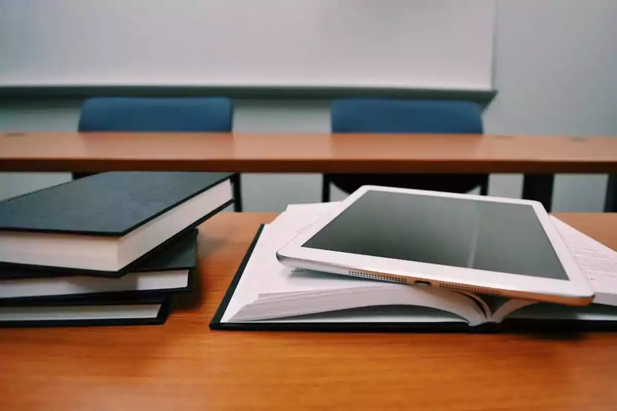 Libros y una tableta sobre un escritorio en un aula de clases.