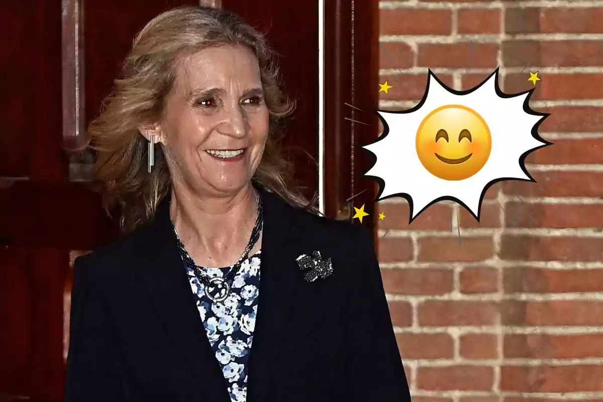 La infanta Elena de cabello rubio sonriente con un emoji de carita feliz sobre un fondo de ladrillos
