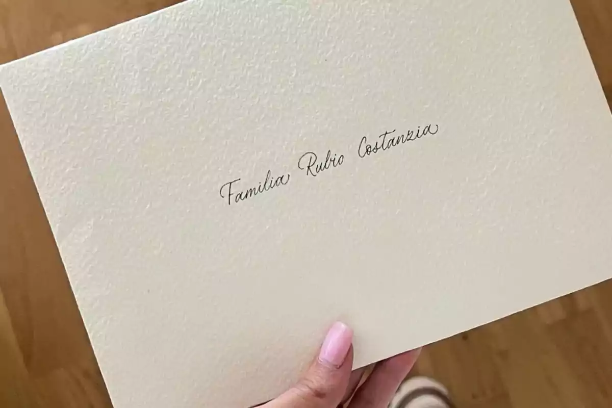 Una mano sostiene un sobre de papel texturizado con un nombre escrito en caligrafía elegante. Una mano sostiene un sobre de papel texturizado con un nombre escrito en caligrafía elegante.