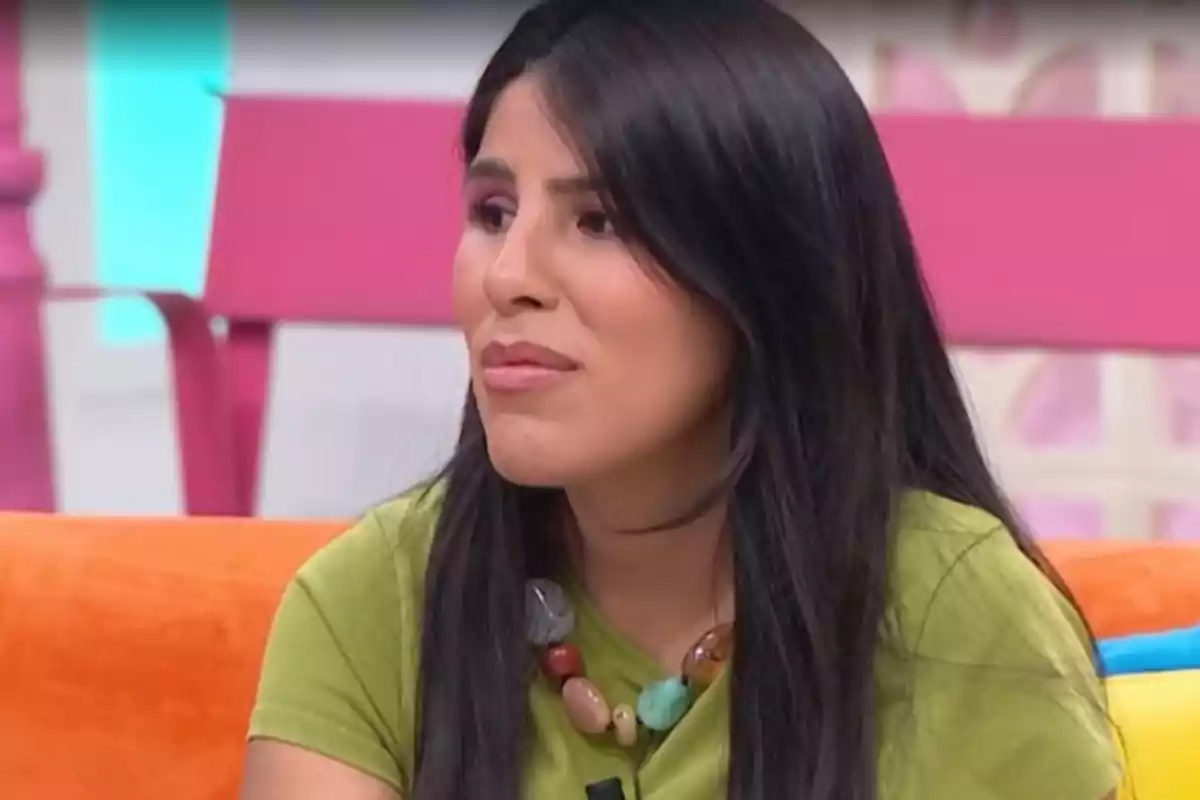 Isa Pantoja con cabello largo y oscuro está sentada en un sofá colorido, lleva una camiseta verde y un collar de cuentas grandes, el fondo es de colores brillantes. Isa Pantoja con cabello largo y oscuro está sentada en un sofá colorido, lleva una camiseta verde y un collar de cuentas grandes, el fondo es de colores brillantes.