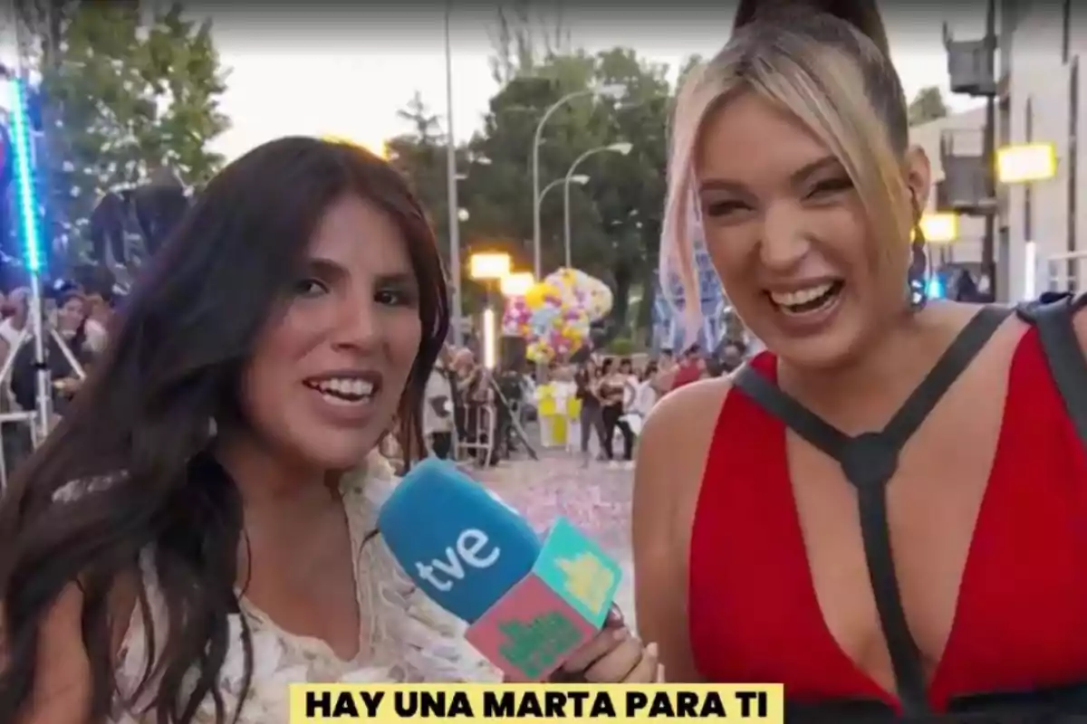 Isa Pantoja y Marta Riesco sonríen mientras una de ellas sostiene un micrófono de TVE en un evento al aire libre con globos y personas de fondo. Isa Pantoja y Marta Riesco sonríen mientras una de ellas sostiene un micrófono de TVE en un evento al aire libre con globos y personas de fondo.