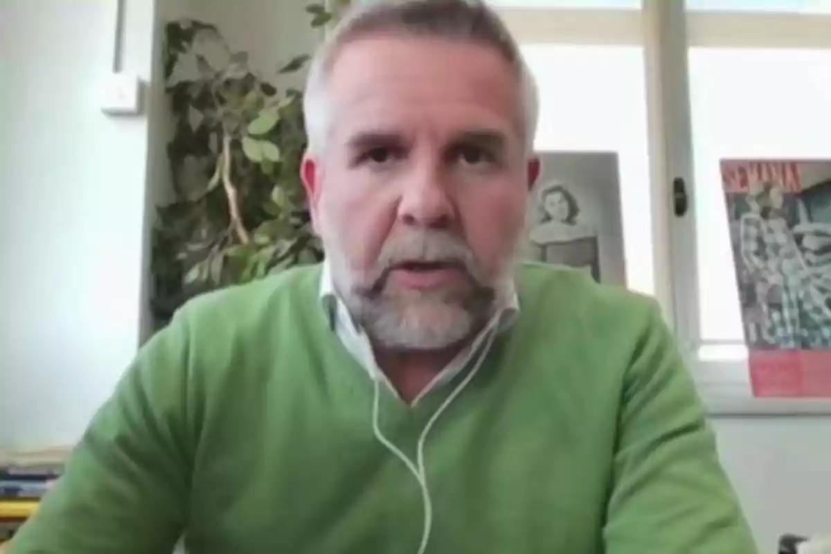 Jorge Borrajo con barba y suéter verde aparece en una videollamada, con un fondo que incluye una planta y carteles en la pared. Jorge Borrajo con barba y suéter verde aparece en una videollamada, con un fondo que incluye una planta y carteles en la pared.