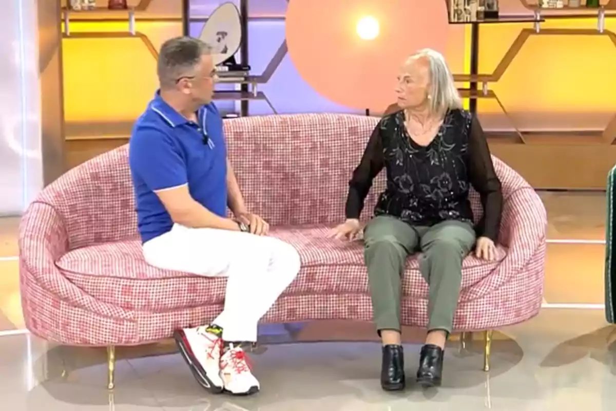 Jorge Javier Vázquez y Lola sentados en un sofá durante un programa de televisión con un fondo iluminado y decorado. Jorge Javier Vázquez y Lola sentados en un sofá durante un programa de televisión con un fondo iluminado y decorado.