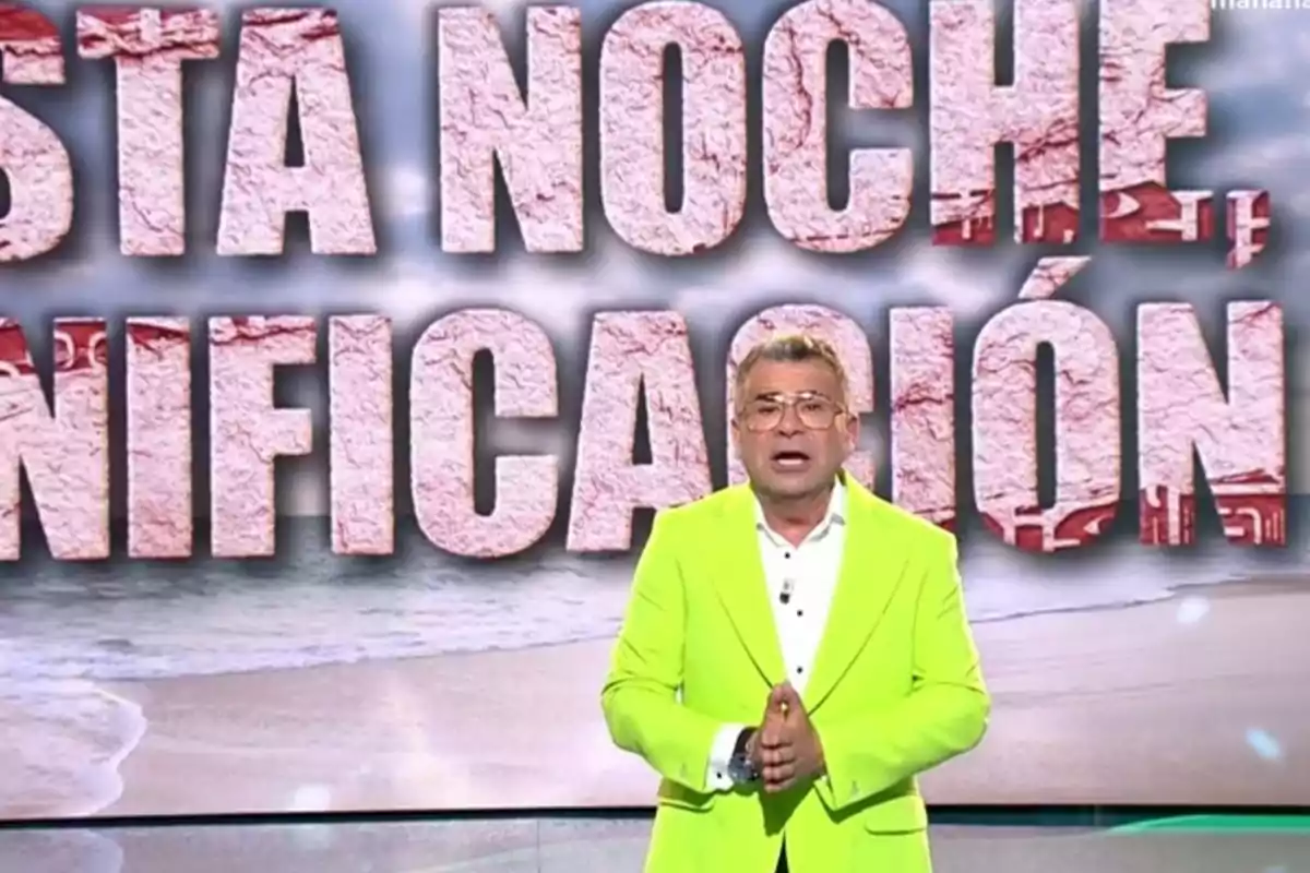 Jorge Javier Vázquez con un traje verde neón está hablando frente a un fondo con letras grandes que dicen Jorge Javier Vázquez con un traje verde neón está hablando frente a un fondo con letras grandes que dicen