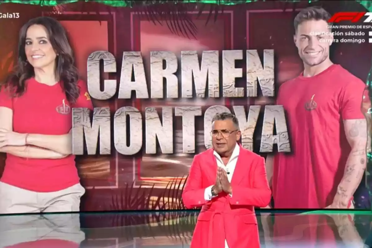 Jorge Javier Vázquez con traje rosa está de pie frente a una pantalla que muestra a Carmen Alcayde y Montoya con camisetas rojas y el texto CARMEN MONTOYA en grande. Jorge Javier Vázquez con traje rosa está de pie frente a una pantalla que muestra a Carmen Alcayde y Montoya con camisetas rojas y el texto CARMEN MONTOYA en grande.