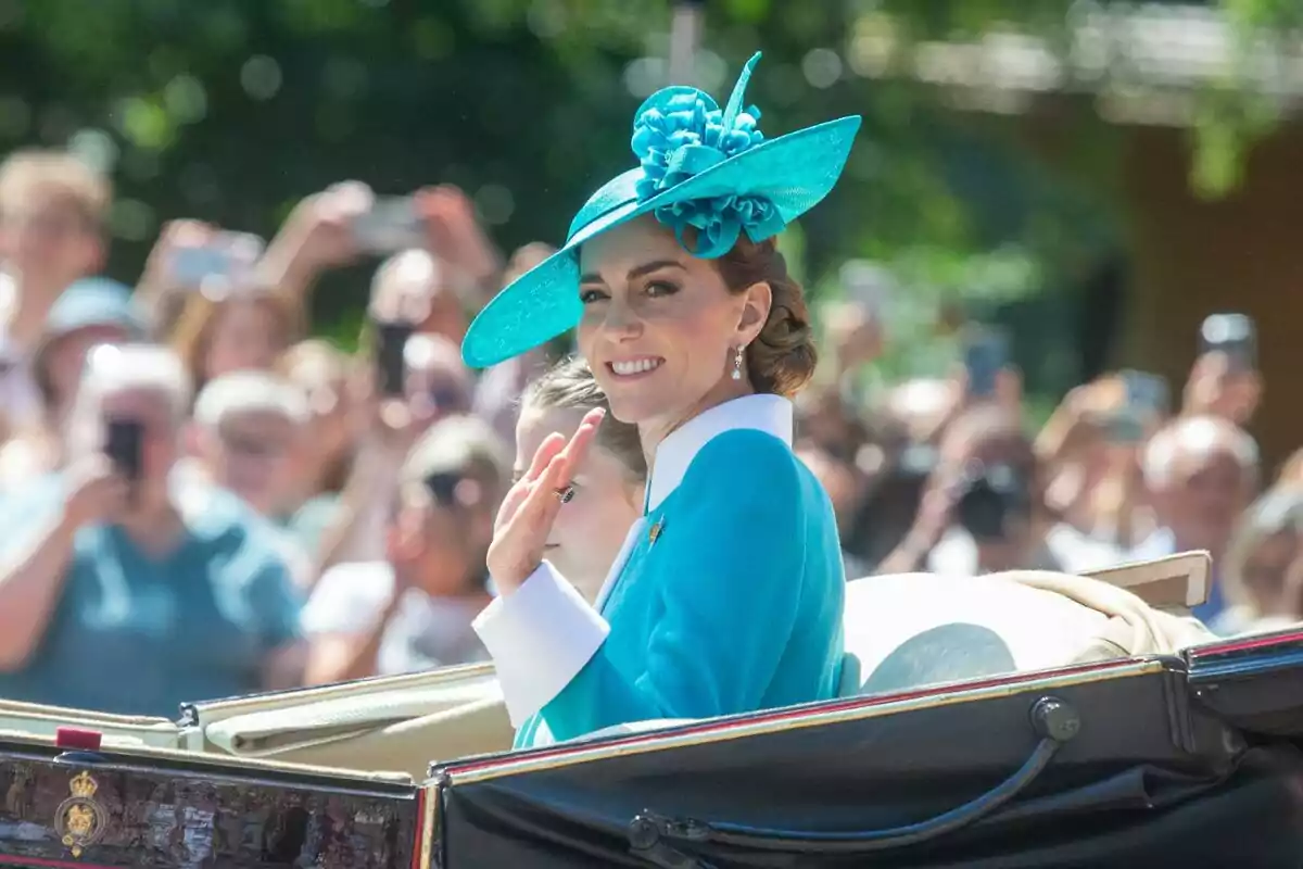Woman in a blue hat smiles and waves from a carriage during an outdoor event with a crowd in the background Woman in a blue hat smiles and waves from a carriage during an outdoor event with a crowd in the background