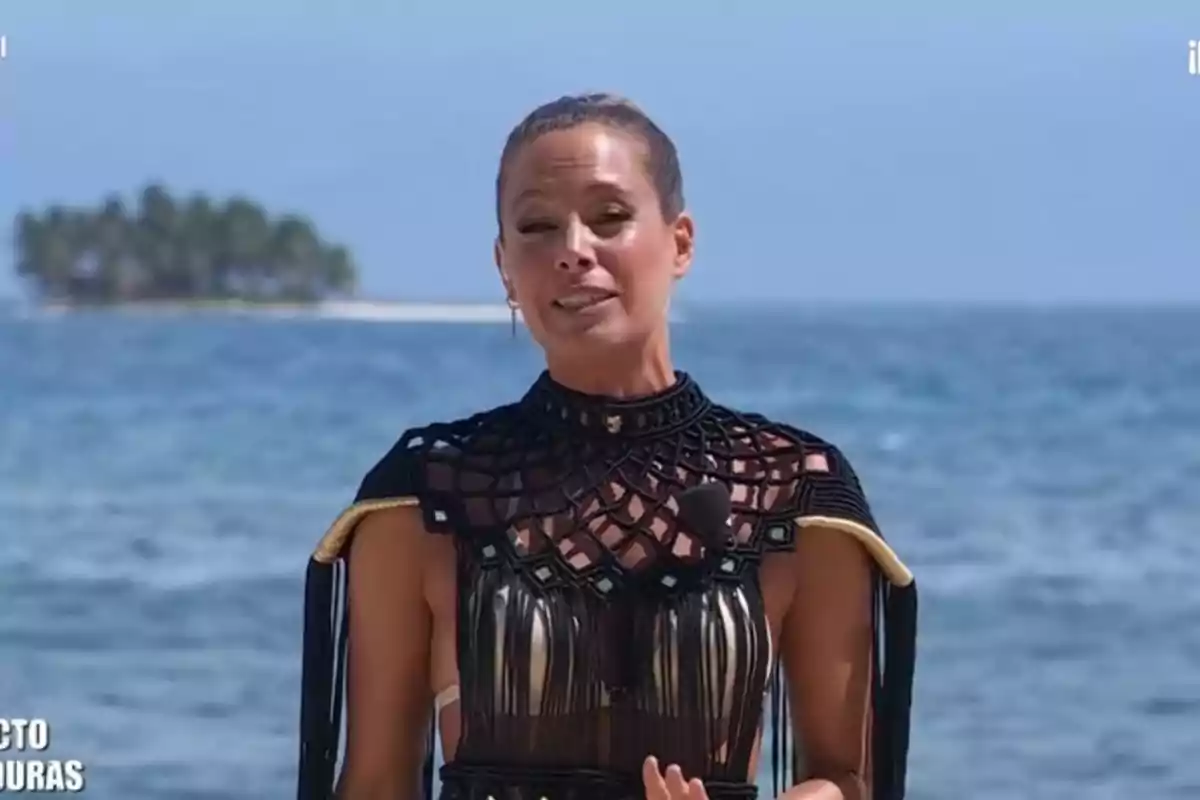 Laura Madrueño de pie frente al mar con una isla al fondo y vistiendo un vestido negro con detalles dorados Laura Madrueño de pie frente al mar con una isla al fondo y vistiendo un vestido negro con detalles dorados