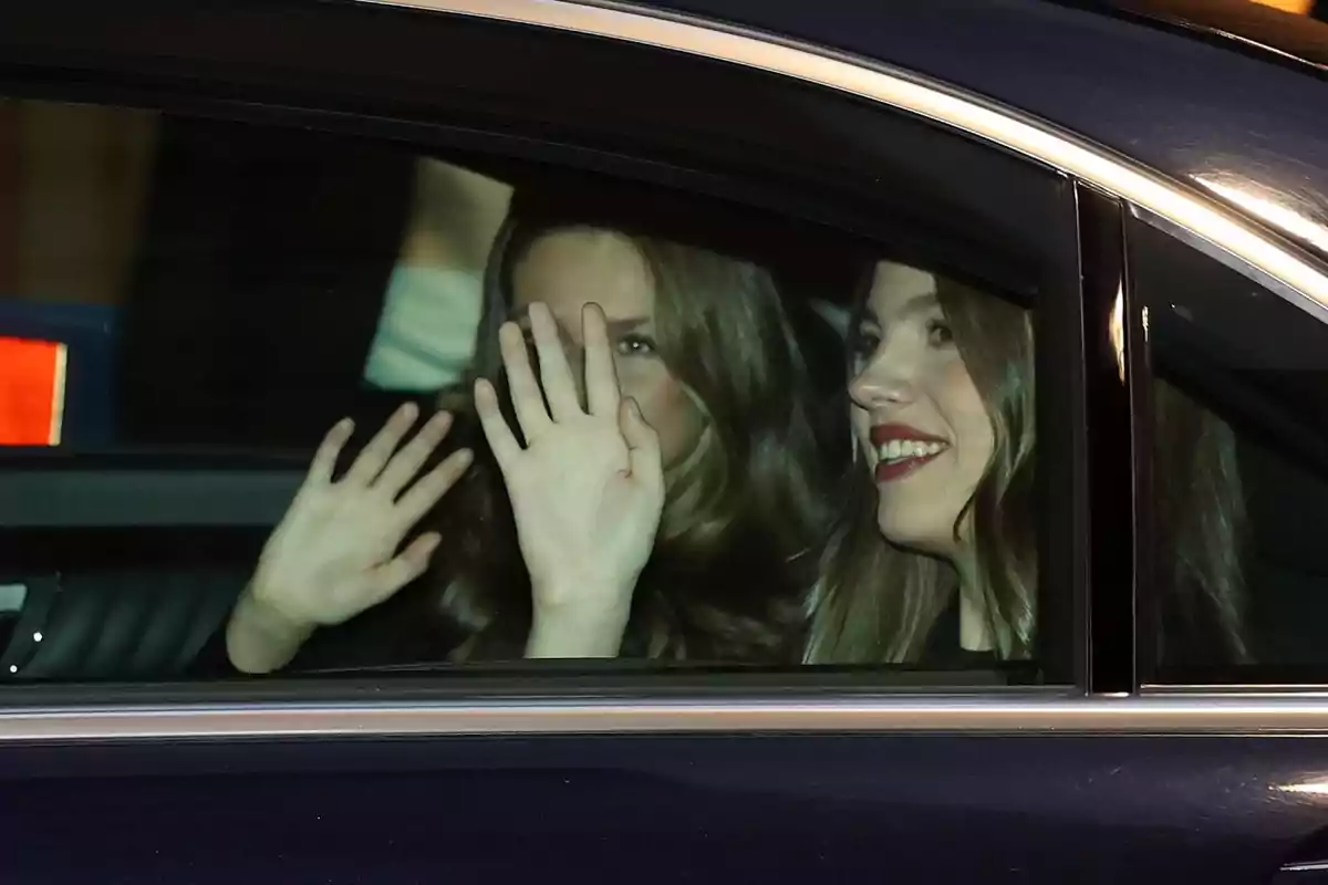 Two people waving from inside a car.