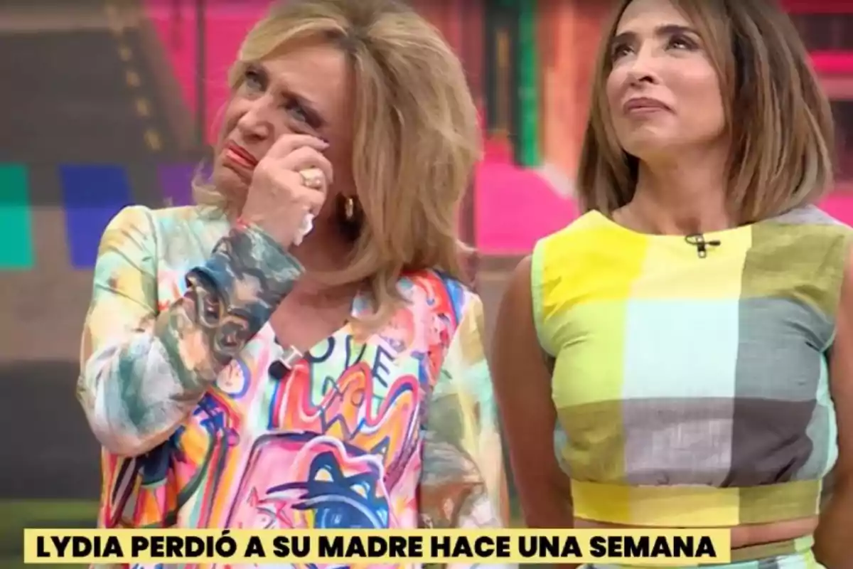 Lydia Lozano y María Patiño en un programa de televisión, Lydia está llorando y María la acompaña, ambas con expresiones serias y fondo colorido. Lydia Lozano y María Patiño en un programa de televisión, Lydia está llorando y María la acompaña, ambas con expresiones serias y fondo colorido.
