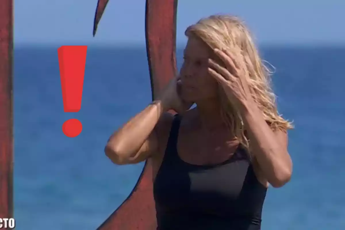 Makoke con cabello rubio y camiseta negra está de pie junto al mar, tocándose el cabello, con un signo de exclamación rojo al lado.
