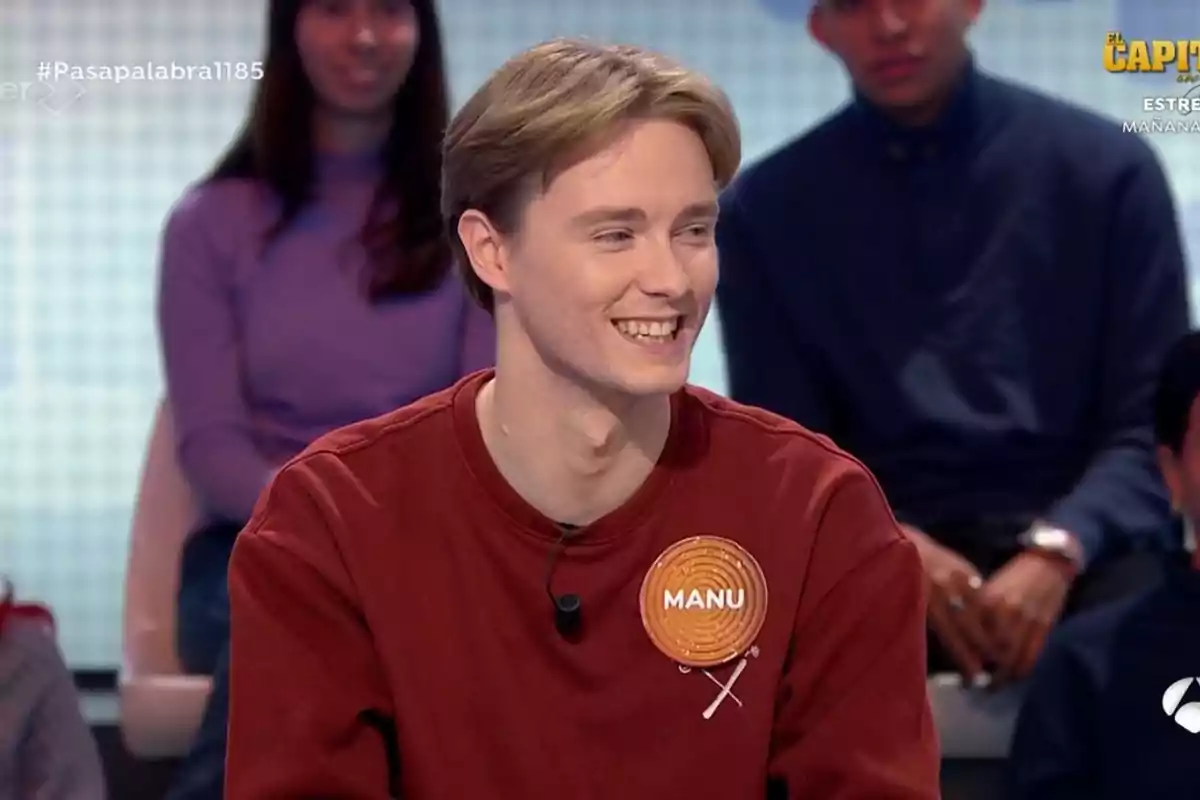 Manu sonriente con un suéter rojo y una etiqueta que dice Manu sonriente con un suéter rojo y una etiqueta que dice