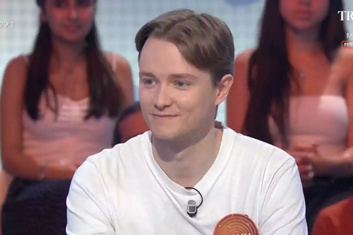 Manu de cabello claro y camiseta blanca participando en un programa de televisión con público al fondo Manu de cabello claro y camiseta blanca participando en un programa de televisión con público al fondo