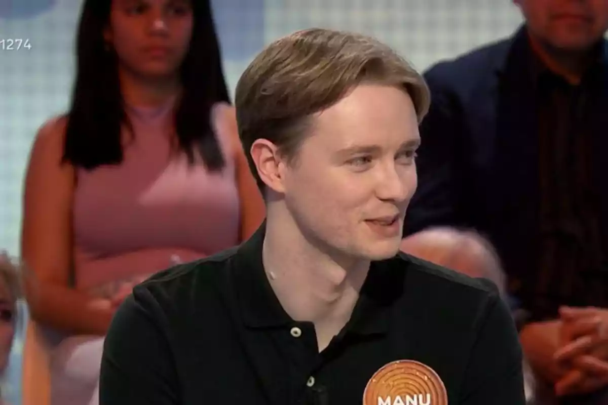 Manu joven con cabello claro y camisa oscura está sentado en un programa de televisión, con personas en el fondo. Manu joven con cabello claro y camisa oscura está sentado en un programa de televisión, con personas en el fondo.