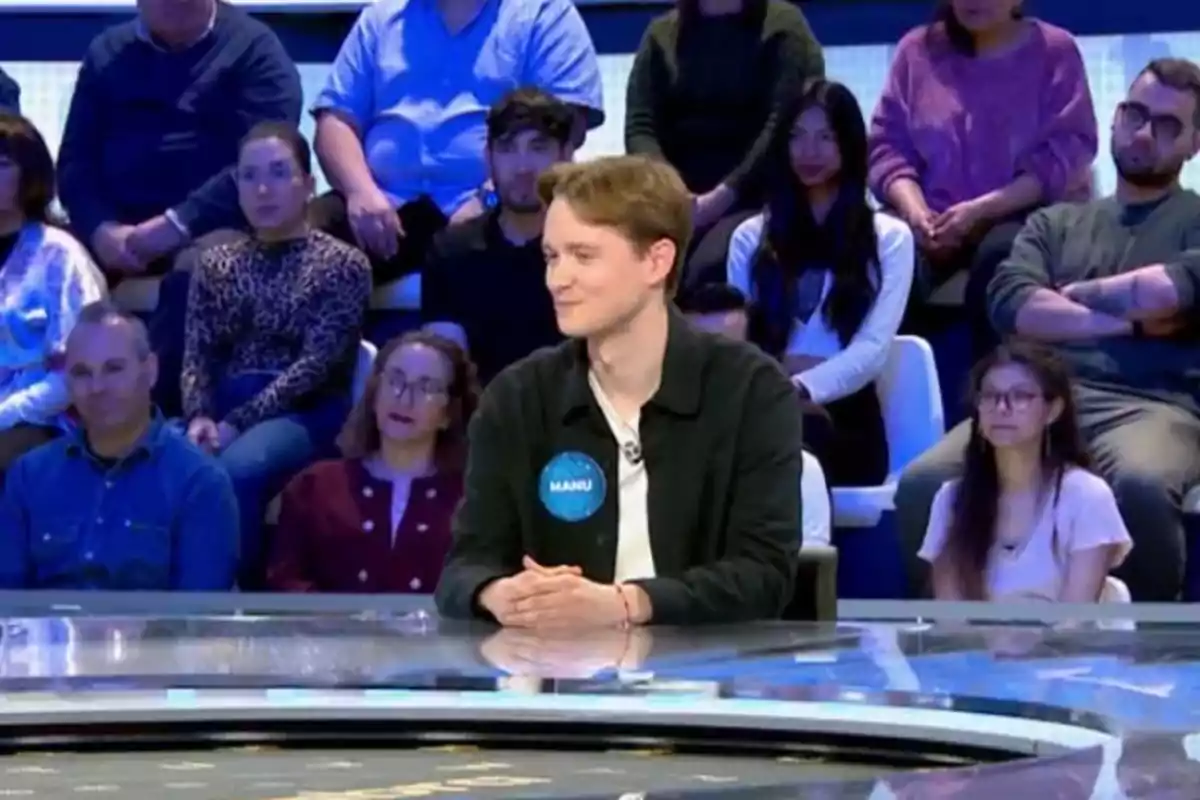 Manu está sentado en un plató de televisión rodeado de público. Manu está sentado en un plató de televisión rodeado de público.