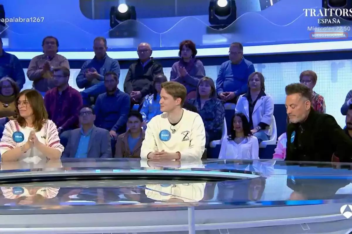Un grupo de personas está sentado en un plató de televisión, con un público al fondo observando. Un grupo de personas está sentado en un plató de televisión, con un público al fondo observando.