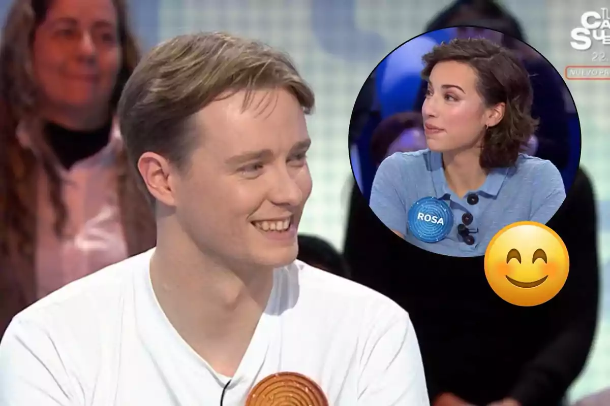 Manu sonriente en un programa de televisión con una imagen insertada de Rosa también en el programa y un emoji sonriente superpuesto.