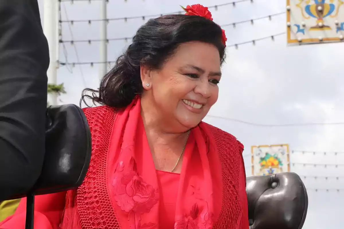 María del Monte sonriente con un vestido rojo y una flor en el cabello, en un ambiente festivo al aire libre. María del Monte sonriente con un vestido rojo y una flor en el cabello, en un ambiente festivo al aire libre.