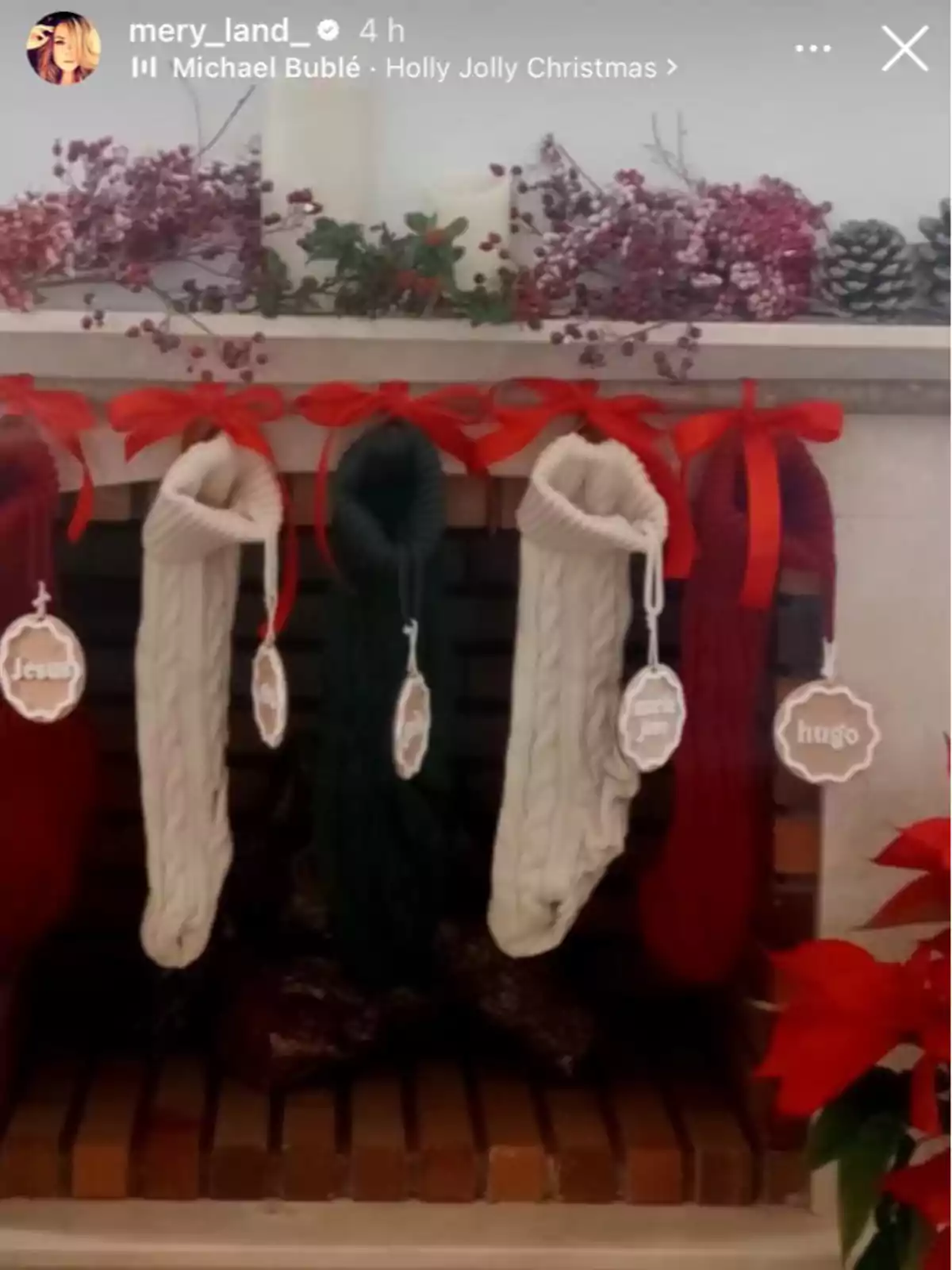 Una chimenea decorada con medias navideñas colgadas y adornos de piñas y flores rojas.