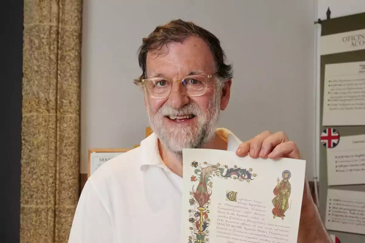 Mariano Rajoy mayor con barba y gafas sonríe mientras sostiene un diploma decorado Mariano Rajoy mayor con barba y gafas sonríe mientras sostiene un diploma decorado