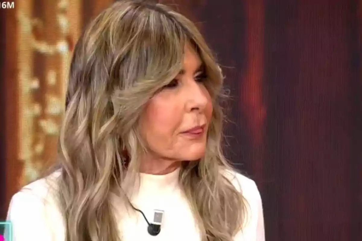 Marisa Martín-Blázquez con cabello largo y rubio ceniza, vestida con una blusa blanca, está participando en un programa de televisión. Marisa Martín-Blázquez con cabello largo y rubio ceniza, vestida con una blusa blanca, está participando en un programa de televisión.