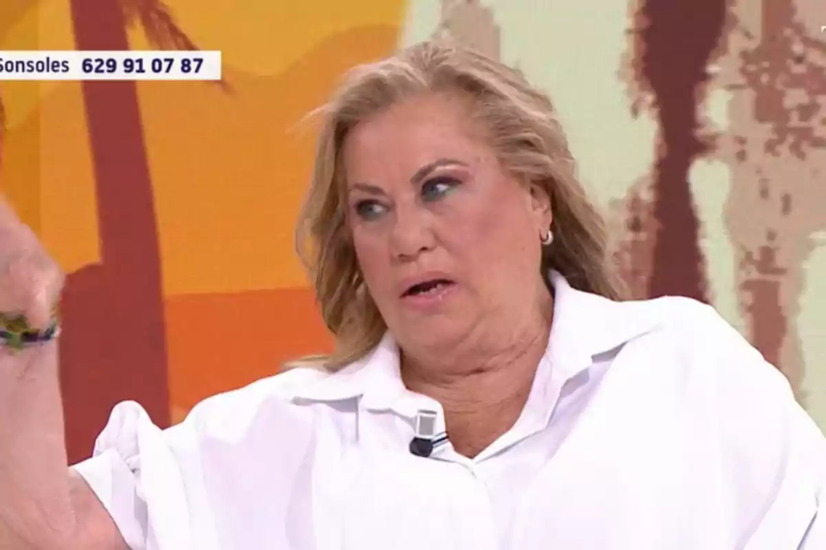Mayte Zaldívar con cabello rubio y camisa blanca está hablando en un programa de televisión con un fondo colorido. Mayte Zaldívar con cabello rubio y camisa blanca está hablando en un programa de televisión con un fondo colorido.