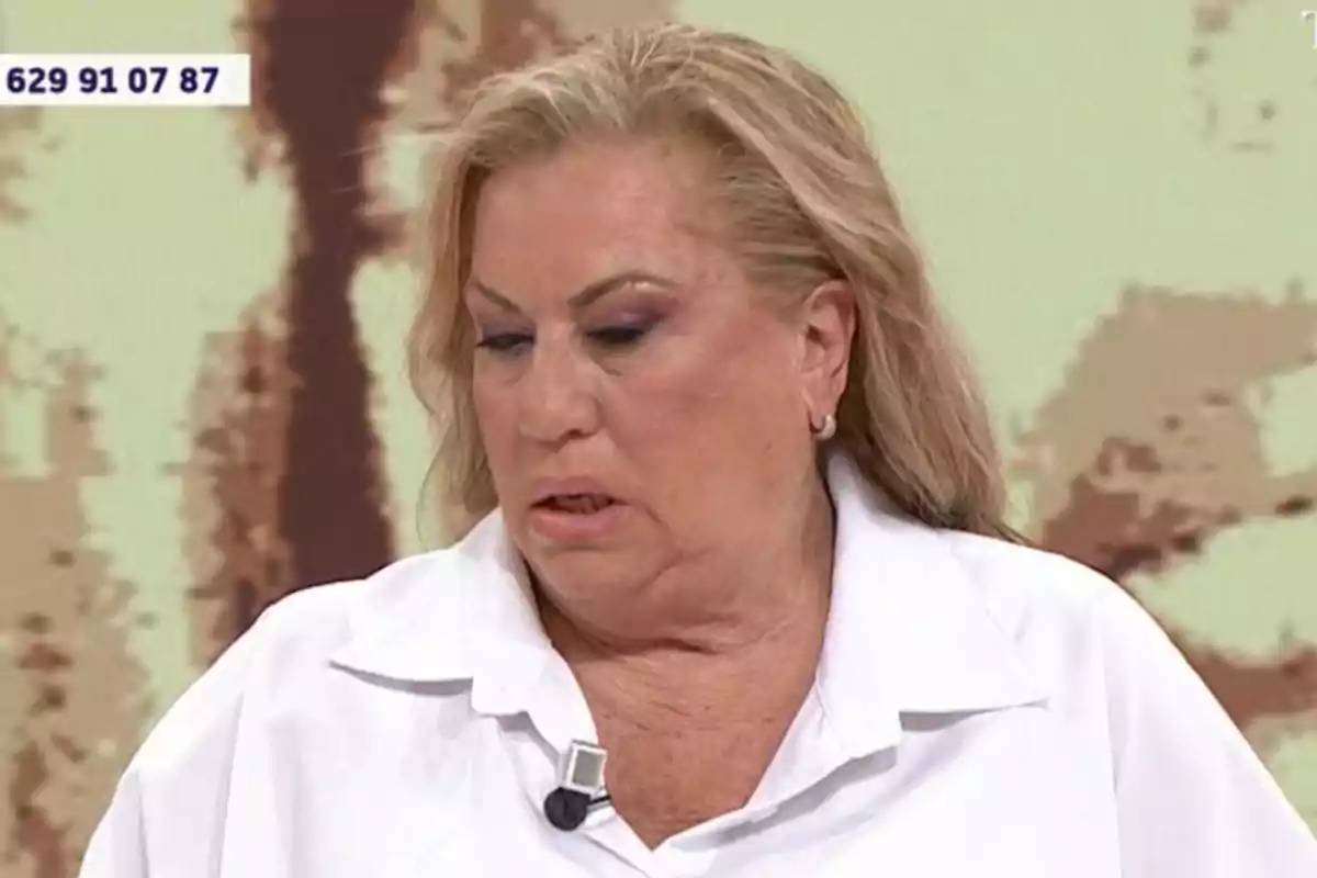 Mayte Zaldívar con cabello rubio y maquillaje pronunciado, vistiendo una camisa blanca y un micrófono de solapa, aparece en un entorno de estudio de televisión con un número de teléfono visible en la esquina superior izquierda. Mayte Zaldívar con cabello rubio y maquillaje pronunciado, vistiendo una camisa blanca y un micrófono de solapa, aparece en un entorno de estudio de televisión con un número de teléfono visible en la esquina superior izquierda.