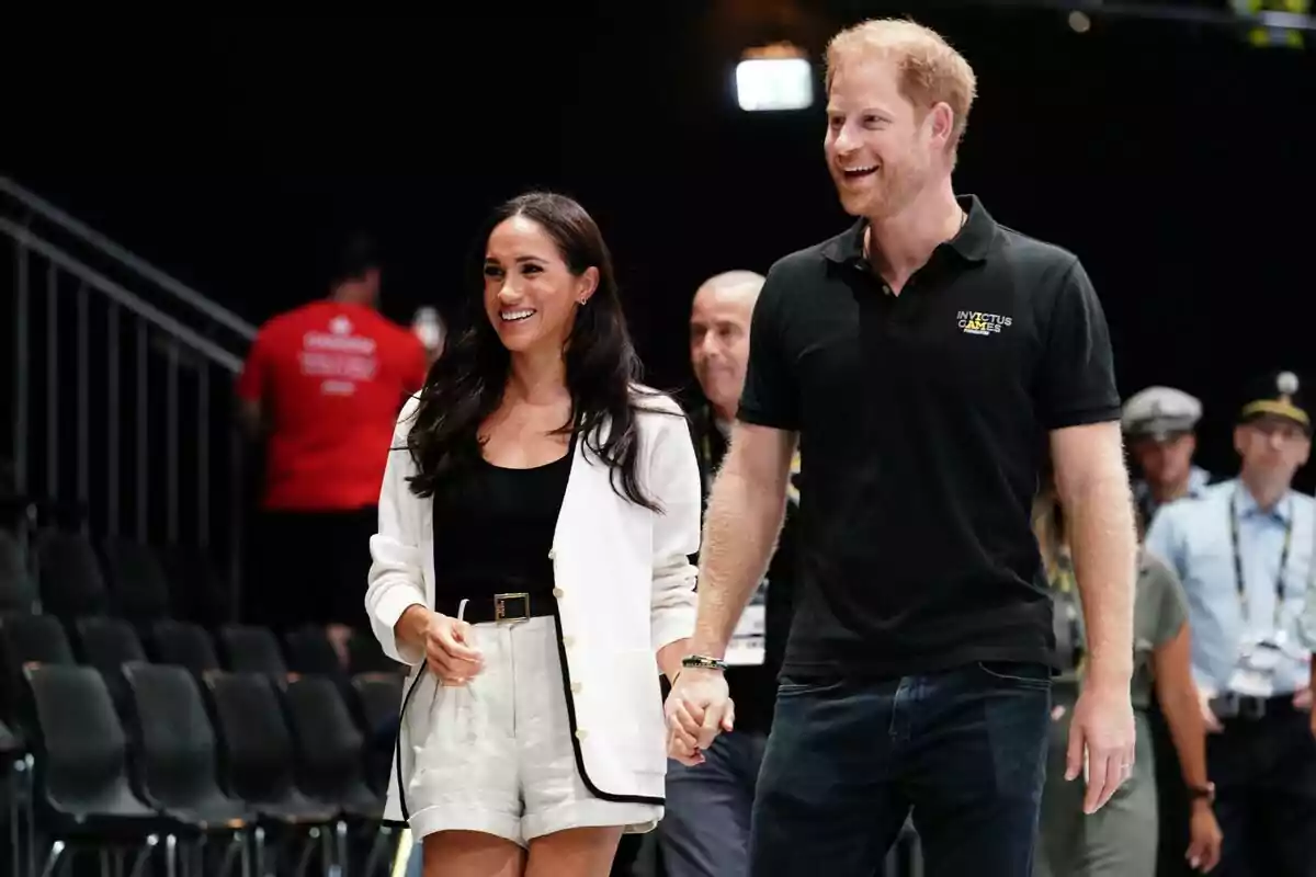 A smiling couple walks hand in hand at a sporting event with people in the background. A smiling couple walks hand in hand at a sporting event with people in the background.