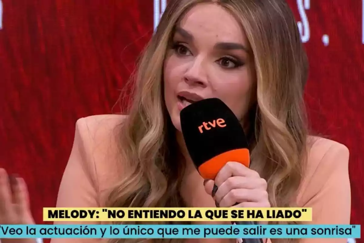 Melody de cabello largo y rubio hablando en una entrevista mientras sostiene un micrófono de rtve, con un fondo rojo y subtítulos en la parte inferior. Melody de cabello largo y rubio hablando en una entrevista mientras sostiene un micrófono de rtve, con un fondo rojo y subtítulos en la parte inferior.