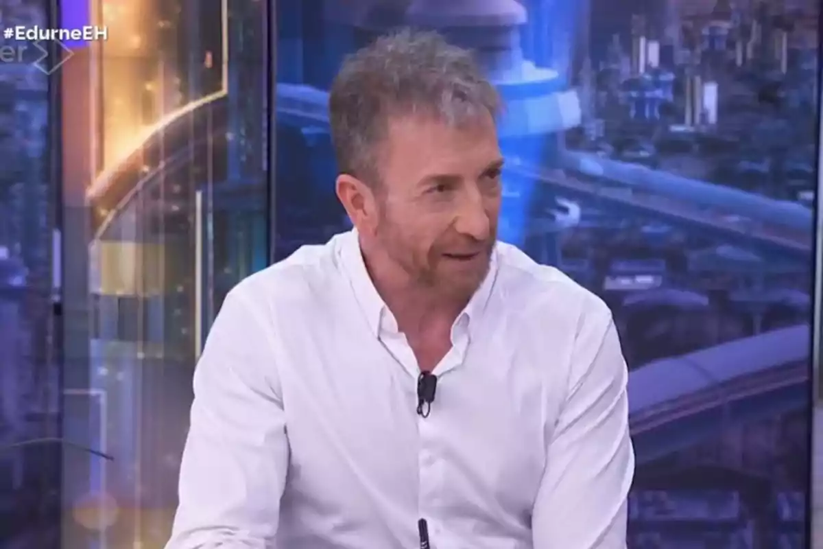 Pablo Motos con camisa blanca está hablando en un programa de televisión con un fondo urbano iluminado. Pablo Motos con camisa blanca está hablando en un programa de televisión con un fondo urbano iluminado.
