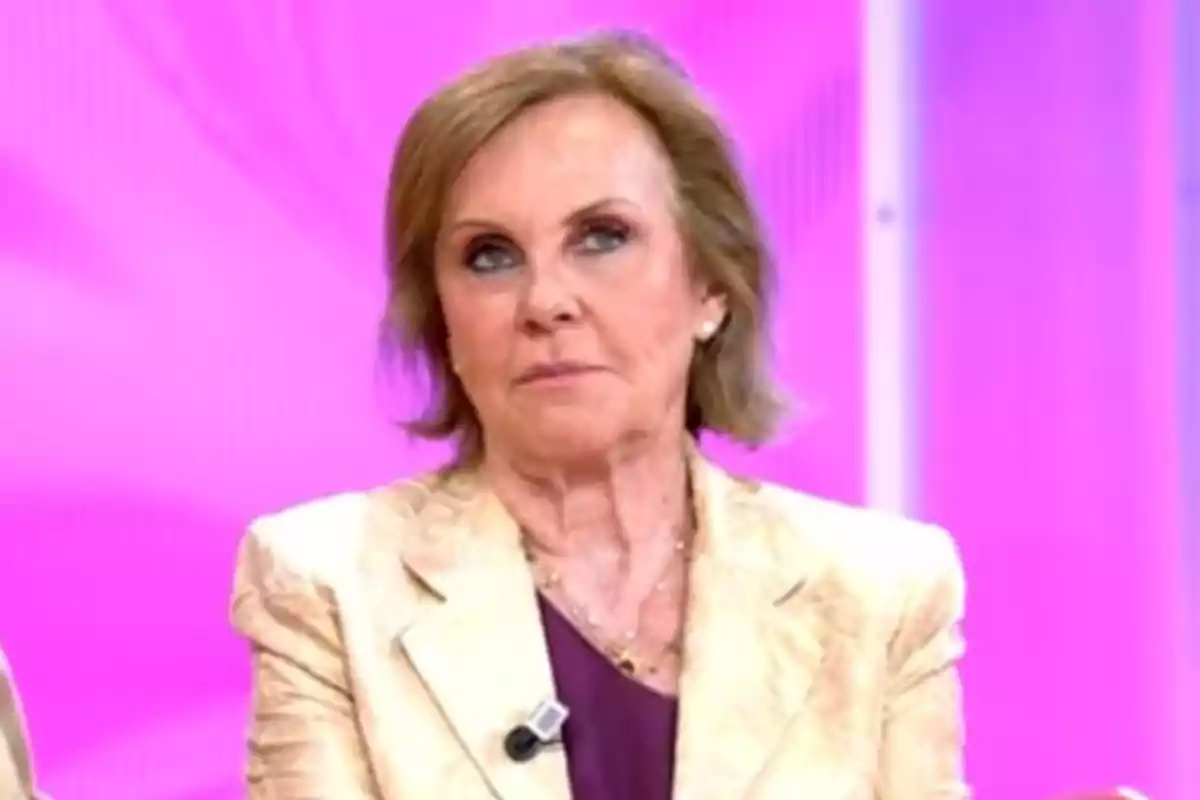 Paloma Barrientos de cabello corto y rubio vestida con un traje claro y blusa oscura, con un micrófono en la solapa, sobre un fondo rosa. Paloma Barrientos de cabello corto y rubio vestida con un traje claro y blusa oscura, con un micrófono en la solapa, sobre un fondo rosa.