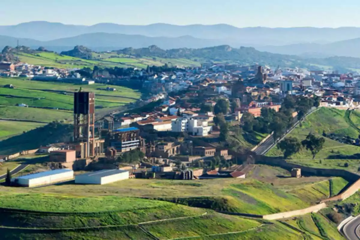 Vista panorámica de Almadén con edificios industriales y casas rodeadas de colinas verdes y montañas al fondo.