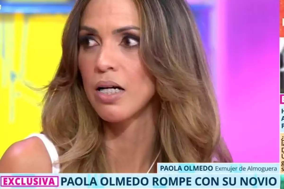 Paola Olmedo de cabello largo y ondulado con expresión de sorpresa durante una entrevista en un programa de televisión, con un cintillo informativo que anuncia una noticia exclusiva sobre su ruptura amorosa. Paola Olmedo de cabello largo y ondulado con expresión de sorpresa durante una entrevista en un programa de televisión, con un cintillo informativo que anuncia una noticia exclusiva sobre su ruptura amorosa.