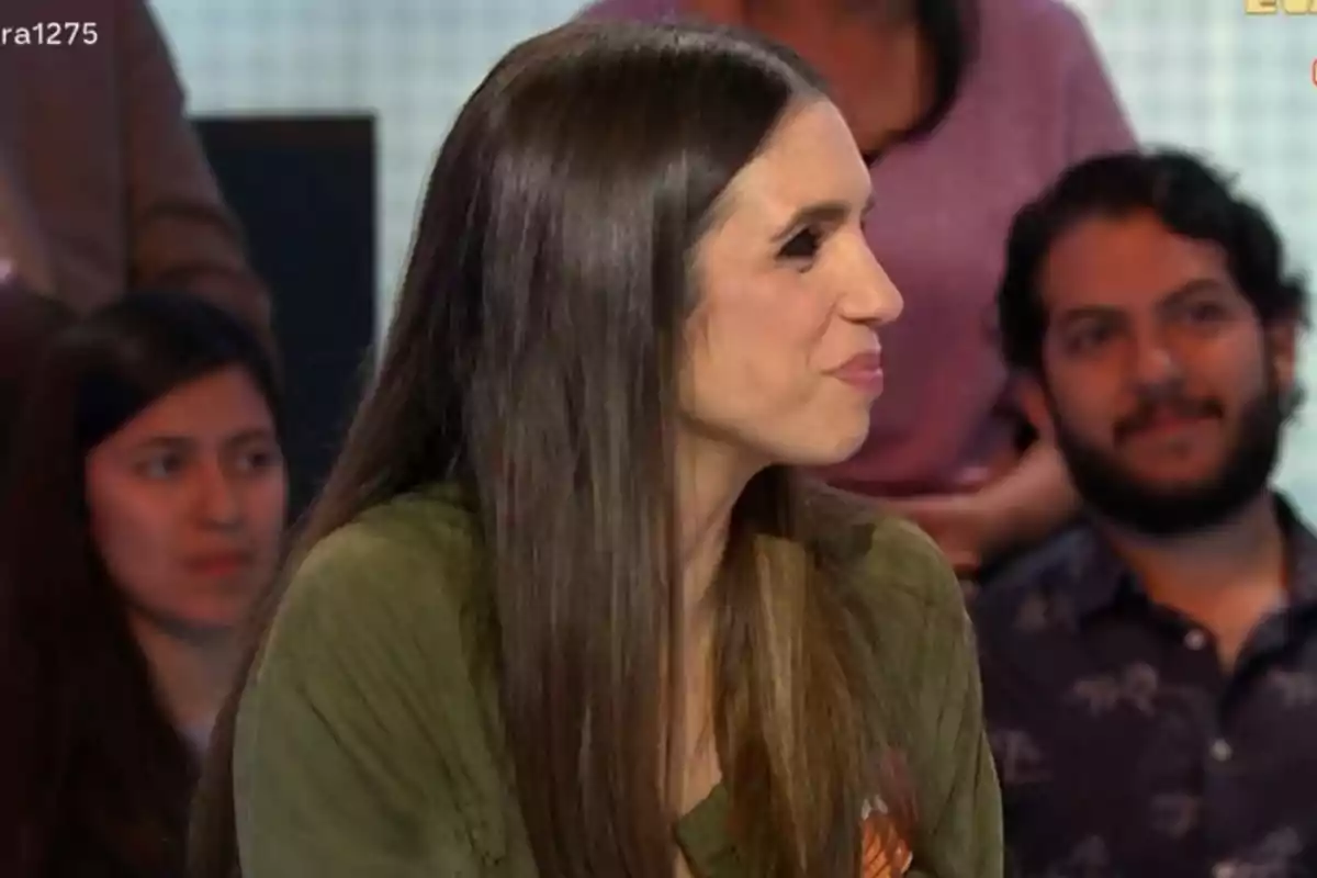 Elena Furiase de cabello largo y oscuro está sentada de perfil en un entorno de estudio con personas al fondo. Elena Furiase de cabello largo y oscuro está sentada de perfil en un entorno de estudio con personas al fondo.