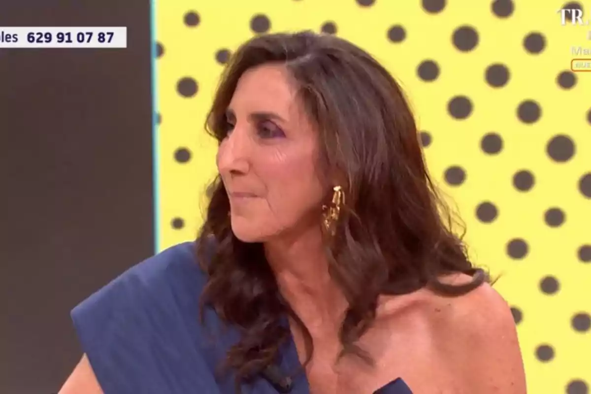 Paz Padilla con cabello largo y oscuro lleva un vestido azul y pendientes dorados, con un fondo amarillo de lunares negros. Paz Padilla con cabello largo y oscuro lleva un vestido azul y pendientes dorados, con un fondo amarillo de lunares negros.