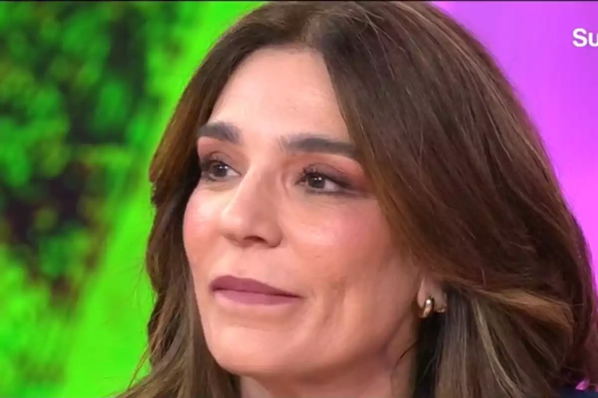 Raquel Bollo con cabello castaño y maquillaje sutil mira hacia un lado con una expresión serena mientras el fondo muestra colores vibrantes. Raquel Bollo con cabello castaño y maquillaje sutil mira hacia un lado con una expresión serena mientras el fondo muestra colores vibrantes.