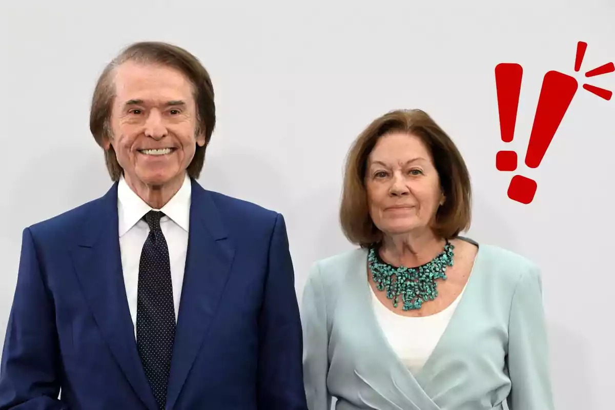 Raphael y Natalia Figueroa posan juntos, una de ellas lleva un traje azul y la otra un conjunto claro con un collar turquesa, con un símbolo de exclamación rojo al lado.