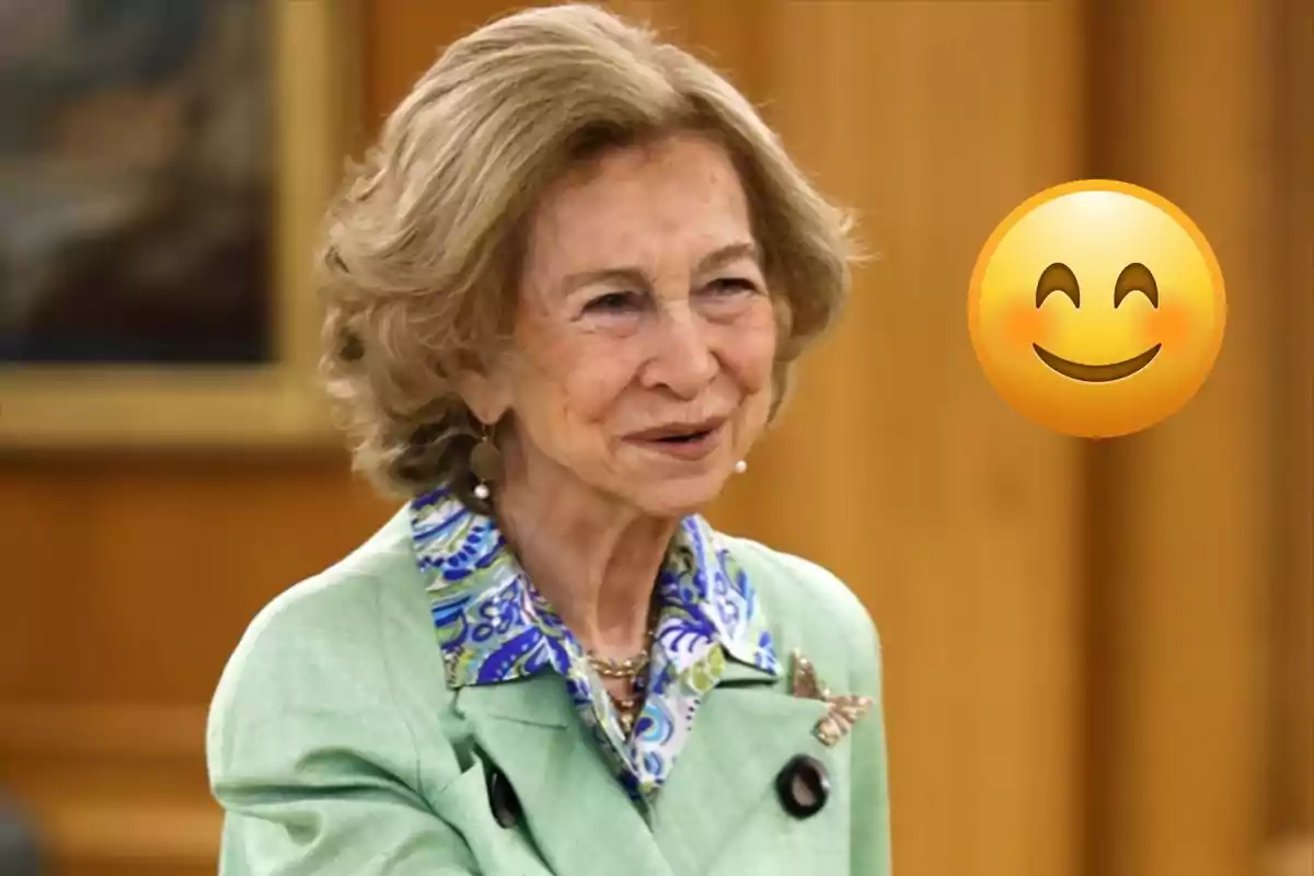 La reina Sofía mayor sonriente con chaqueta verde claro y emoji de carita feliz a su lado