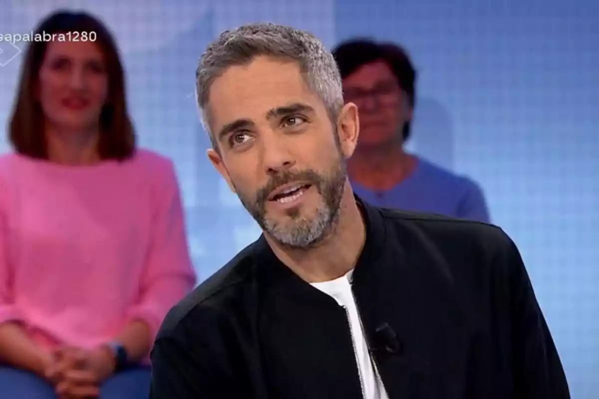 Roberto Leal de cabello corto y barba hablando en un programa de televisión con dos personas sentadas al fondo Roberto Leal de cabello corto y barba hablando en un programa de televisión con dos personas sentadas al fondo