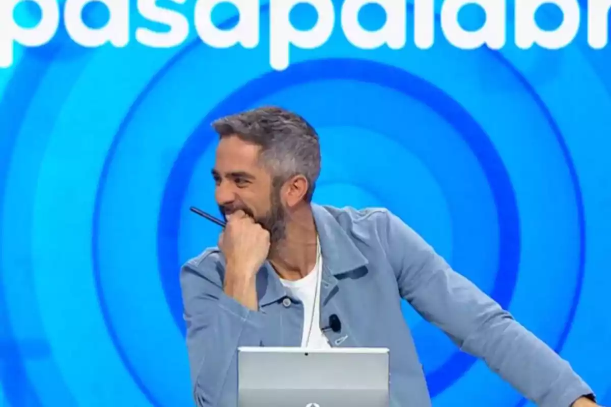 Roberto Leal sonriendo y apoyado en un escritorio con fondo azul y letras blancas. Roberto Leal sonriendo y apoyado en un escritorio con fondo azul y letras blancas.