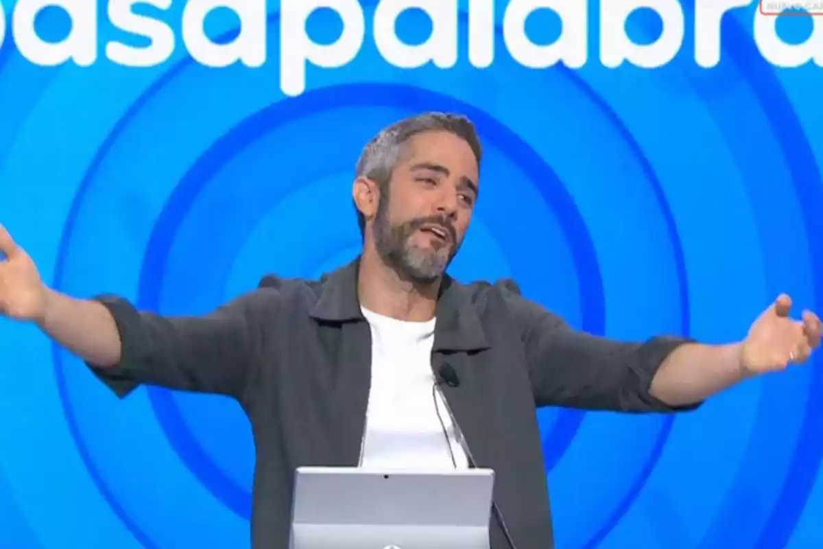 Roberto Leal de cabello y barba canosa con los brazos extendidos en un set de televisión con fondo azul y letras blancas Roberto Leal de cabello y barba canosa con los brazos extendidos en un set de televisión con fondo azul y letras blancas