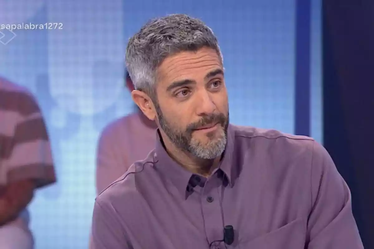 Roberto Leal con barba y cabello canoso, vestido con una camisa morada, está sentado en un estudio de televisión. Roberto Leal con barba y cabello canoso, vestido con una camisa morada, está sentado en un estudio de televisión.