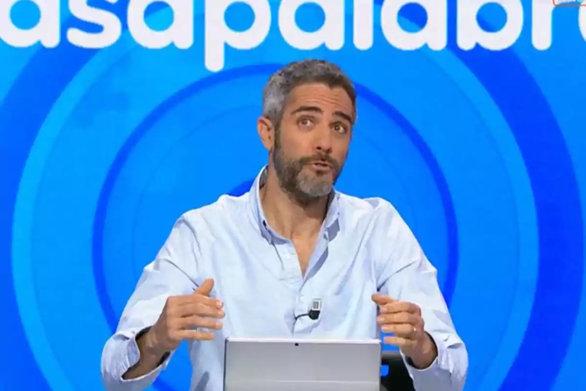 Roberto Leal de cabello corto y barba hablando en un set de televisión con fondo azul y letras blancas Roberto Leal de cabello corto y barba hablando en un set de televisión con fondo azul y letras blancas