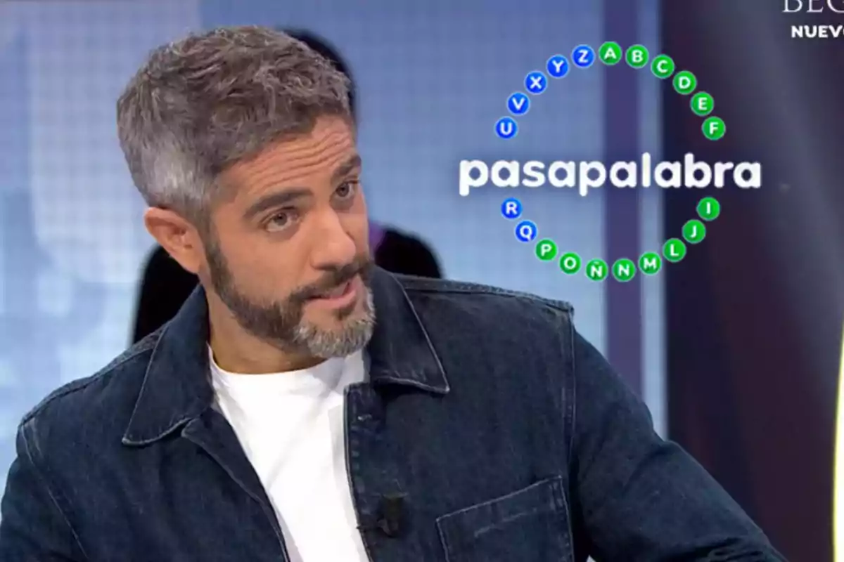 Roberto Leal con barba y cabello canoso está en un programa de televisión llamado "Pasapalabra" con un gráfico de letras en círculo a su lado.