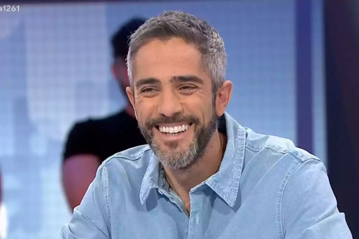 Roberto Leal sonriente con barba y camisa de mezclilla en un estudio de televisión. Roberto Leal sonriente con barba y camisa de mezclilla en un estudio de televisión.