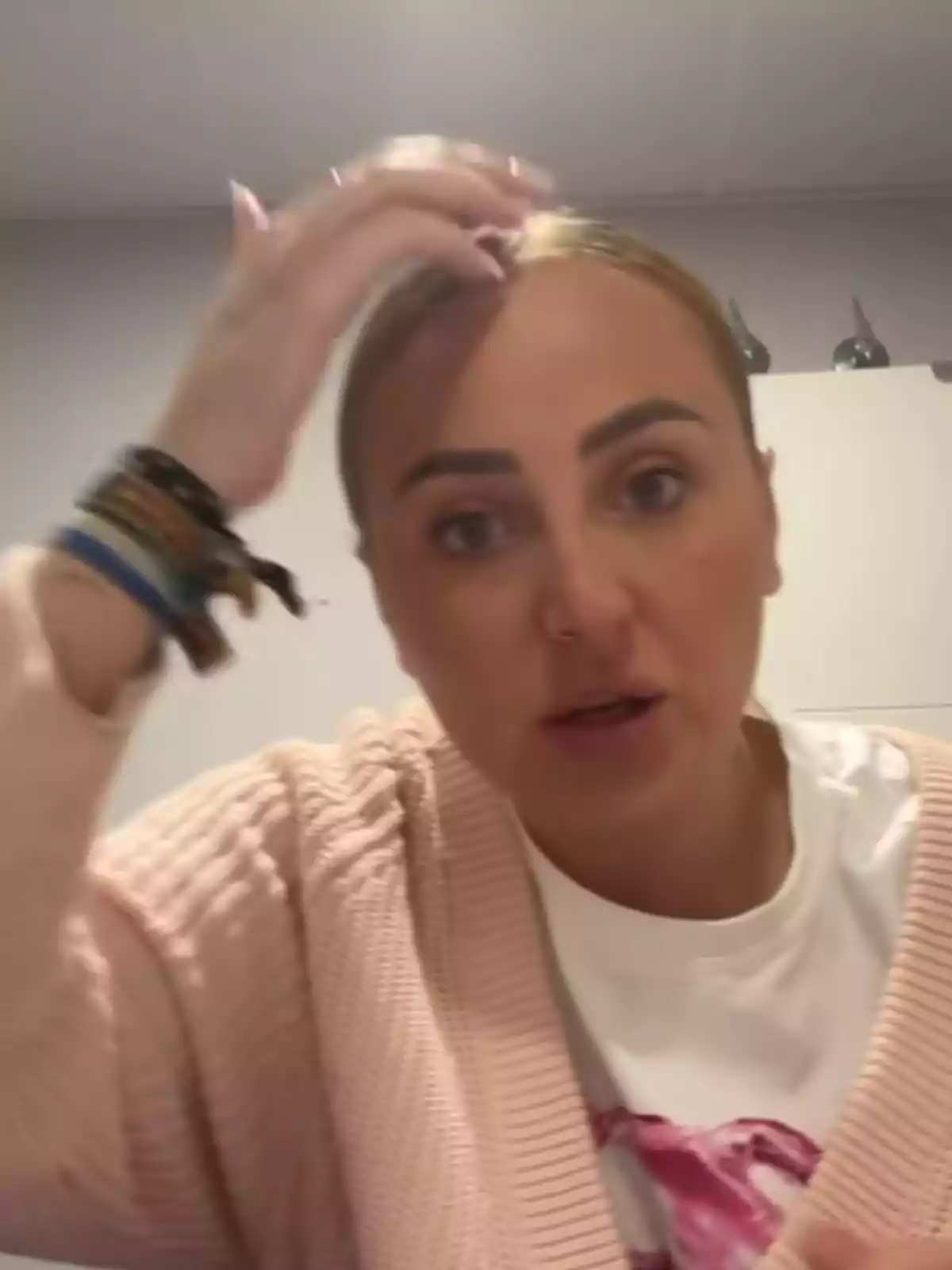 Rocío Flores con cabello recogido y suéter rosado se toca la cabeza mientras mira hacia la cámara en un ambiente interior. Rocío Flores con cabello recogido y suéter rosado se toca la cabeza mientras mira hacia la cámara en un ambiente interior.